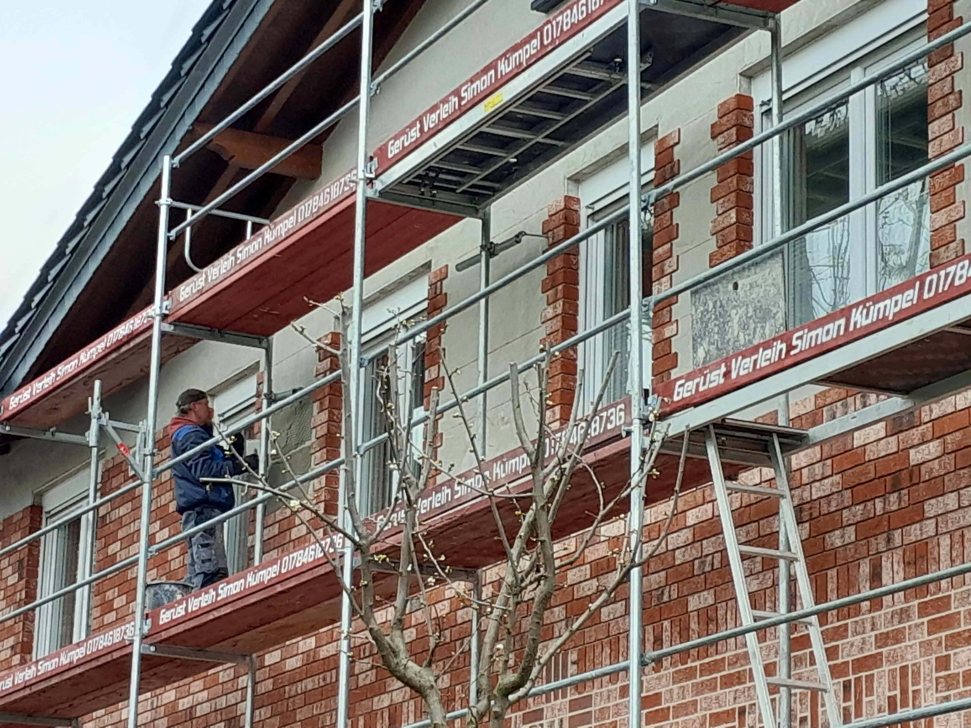 Fassadengerüst mit Gerüstbelägen an einem Klinkerhaus, Monteur bei der Fensterarbeit